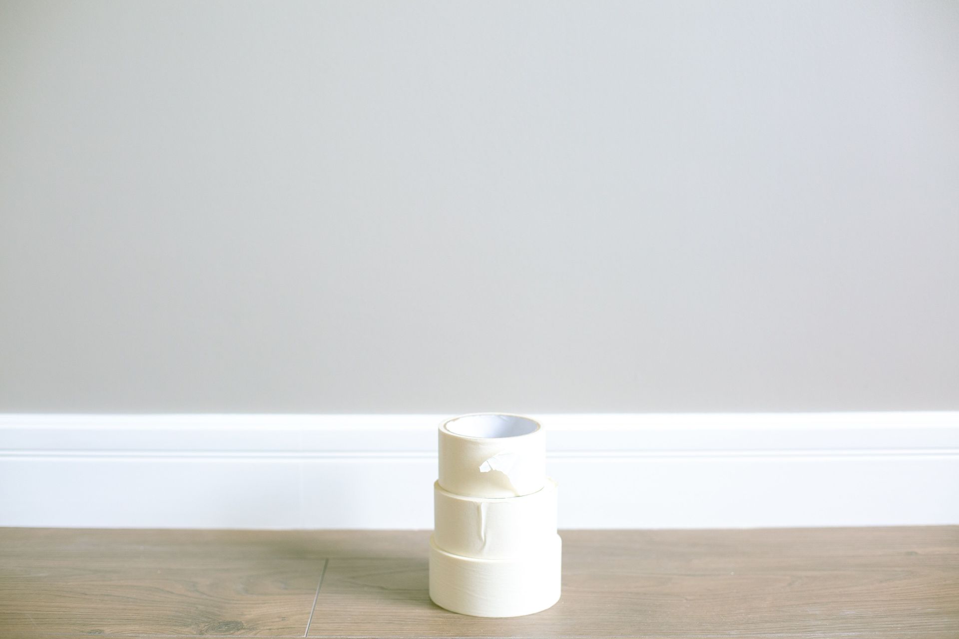 Stack of white masking tape on a wooden floor against a minimal interior wall.