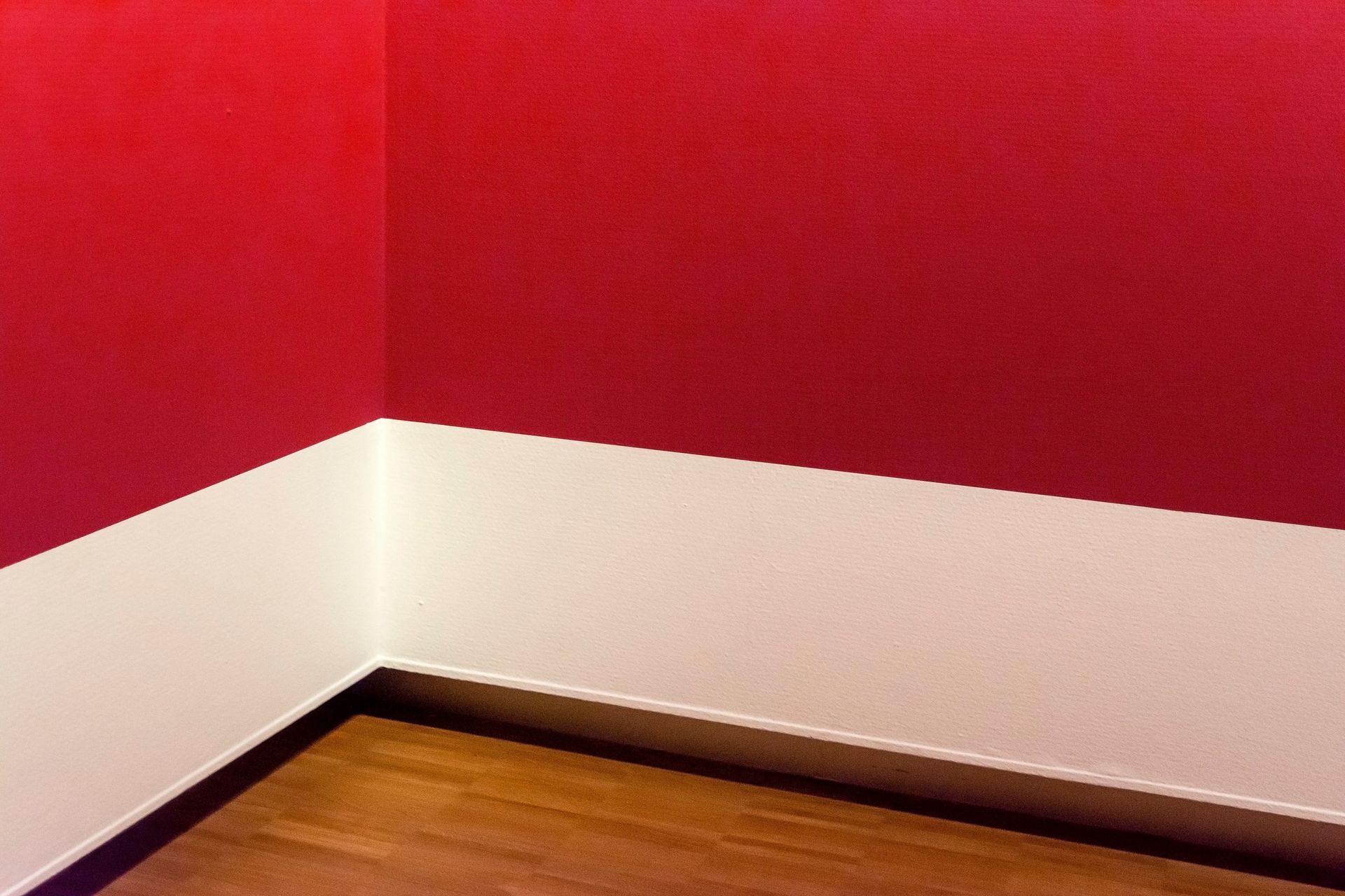 A minimalist room corner with striking red walls and wooden flooring, showcasing modern design.